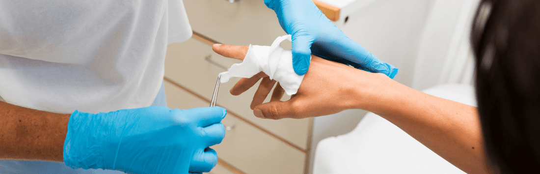 Medizinisches Personal mit blauen Handschuhen versorgt Hand mit Verband und Instrument, Nahaufnahme in Behandlungsumgebung