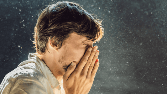 Mann der in einer Staubwolke steht und sich die Hände beim Nießen vor sein Gesicht hält