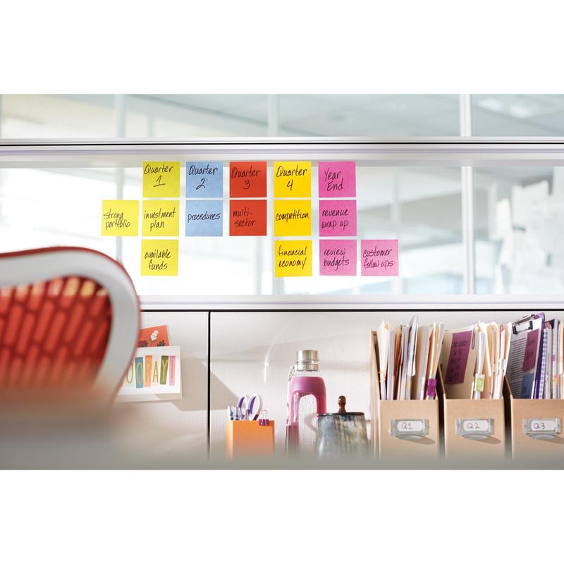 Rivi 3M Deutschland GmbH:n Post-it® Super Sticky Notes -muistilappuja, 76 mm x 76 mm, 90 arkkia/pakkaus, 100% PEFC, on järjestetty lasiväliseinälle toimistossa organisoitujen tarvikkeiden, kansioiden ja kirjojen yläpuolelle, edessä oranssi tuoli.