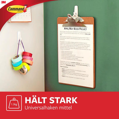 Vihreällä seinällä roikkuu leikekirja, jossa on 3M Deutschland GmbH Keskikokoiset Command™ monikäyttökoukut M edullispakkauksessa, 17001-2. Lähellä roikkuu useita teippirullia. Kuvassa näkyy saksankielinen teksti ja 3M Command-logo.