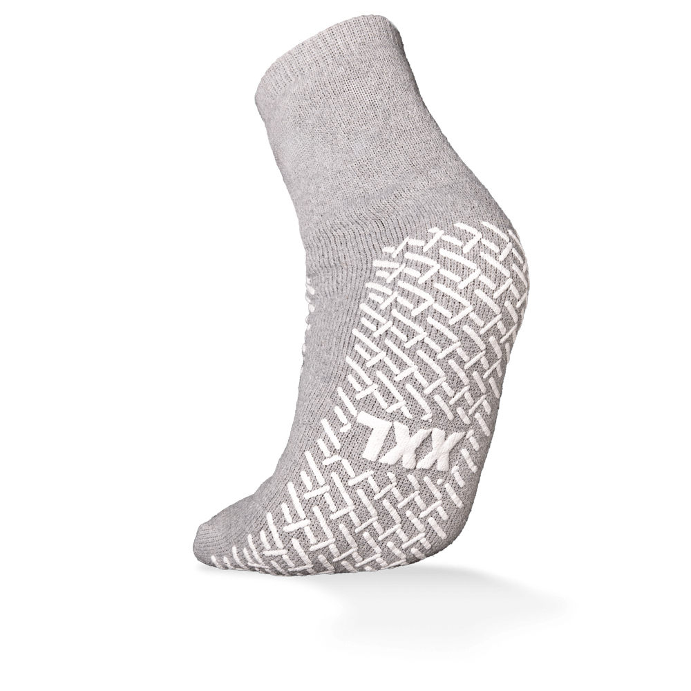 Kuvassa on yksi harmaa ECO-PLUS liukueste kertakäyttösukka AMPri Handelsgesellschaft mbH:ltä, jossa on valkoinen liukueste ja "TXX"-merkintä pohjassa. Molemmin puolin päällystetty, ihanteellinen lääketieteellisiin alueisiin; tausta on yksinkertaisen valkoinen.