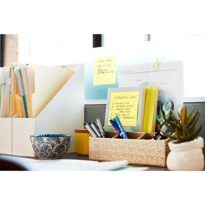 Siisti työpöytä, jossa on kansioita, asiakirjoja, kyniä punotussa säiliössä, koristeellinen kulho, pieni kasvi ja 3M Deutschland GmbH:n Post-it® -muistilappuja suurikokoisena (keltainen, 101x152 mm), yksi tekstillä "Installation Crew", aurinkoisella ikkunalla.