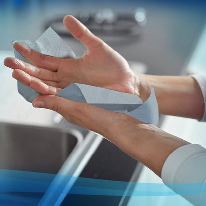 Henkilö kuivaa kätensä Scott® Essential™ käsipyyhkeillä Kimberly-Clark GmbH:lta (rulla / sininen - 6 rullaa) modernissa keittiössä pesualtaan yläpuolella.