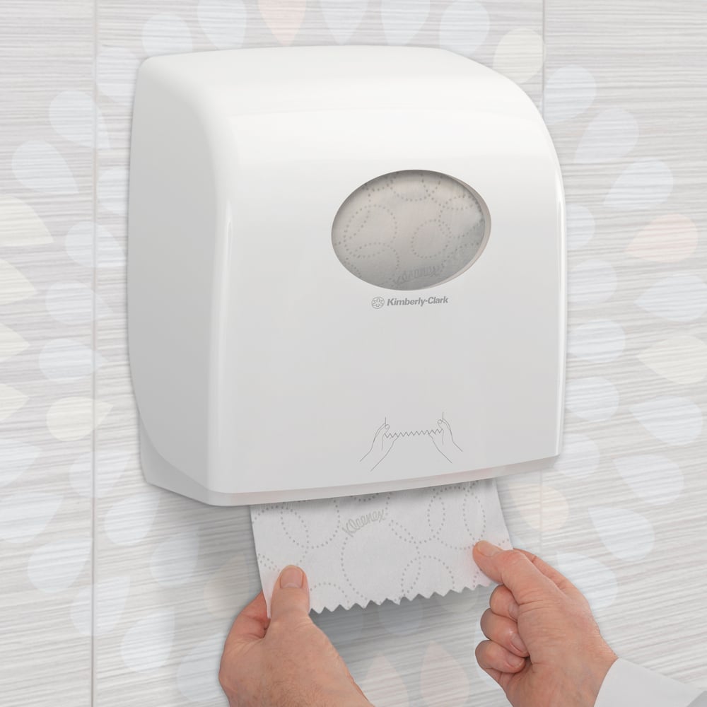 Joku vetää Kleenex® Ultra™ Slimroll™ -käsipyyhkeen seinään kiinnitetystä valkoisesta annostelijasta, jossa on katseluikkuna ja symboleja kaakeloidussa WC:ssä. Tuote: 6-rullan laatikko Kimberly-Clark GmbH:lta.