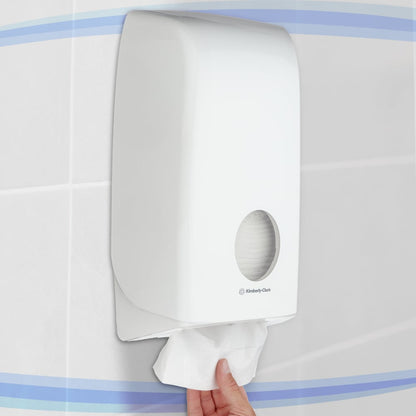 Käsi vetää WC-paperia Kimberly-Clark GmbH:n valkoisesta Aquarius™ WC-paperiannostelijasta, joka on seinään kiinnitetty hygieenistä säilytystä varten kaakeloidussa kylpyhuoneessa.