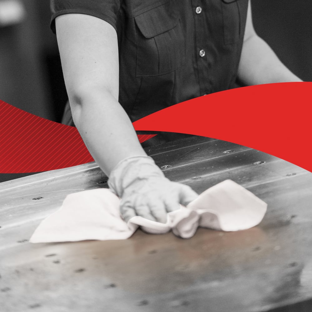 Henkilö lyhythihaisessa paidassa pyyhkii suurta metallipintaa pyyhkeellä, mahdollisesti Kimberly-Clark GmbH:n WypAll® X60 General Clean BRAG™ Boxista (41,80 cm x 28,30 cm); kuva on pääosin mustavalkoinen, ja keskellä on voimakas punainen viisto.