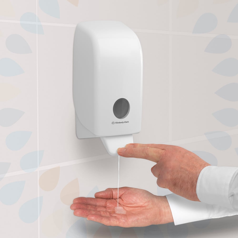 Henkilö painaa seinään kiinnitettyä Kimberly-Clark GmbH:n Kleenex® Extra Gel -käsidesiannostelijaa, joka on kiinnitetty kaakeloituun seinään, ja annostelee käsidesigeeliä 1 litran kasetista avoimeen kämmenelleen.