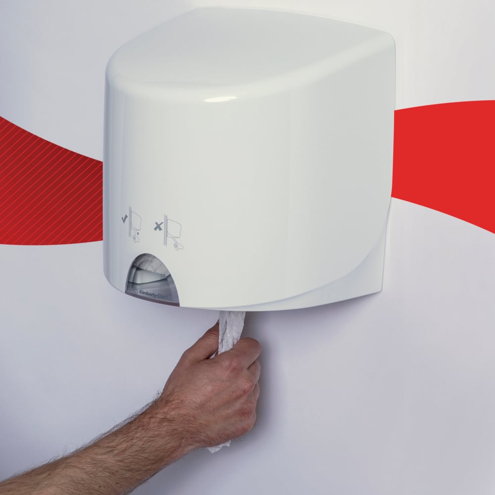 Eine Person zieht ein WypAll® L10 Papierwischtuch der Kimberly-Clark GmbH aus einem weißen, an der Wand montierten Centrefeed for Reach+™-Spender (38,00 cm x 18,30 cm), der mit einem roten Streifen an der Wand befestigt ist.