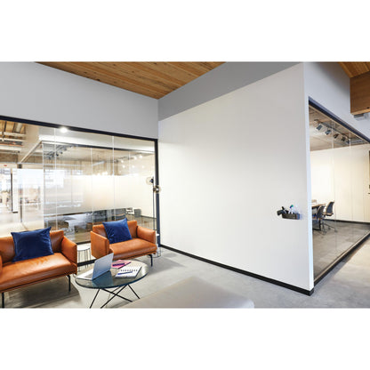 Moderni toimiston odotustila, jossa on kaksi ruskeaa nahkatuolia, sinisiä tyynyjä, lasinen sohvapöytä kannettavan tietokoneen ja muistikirjan kanssa sekä lasiset kokoushuoneet, jotka on varustettu 3M Deutschland GmbH:n Post-it® Easy Erase Whiteboard -pinnalla.