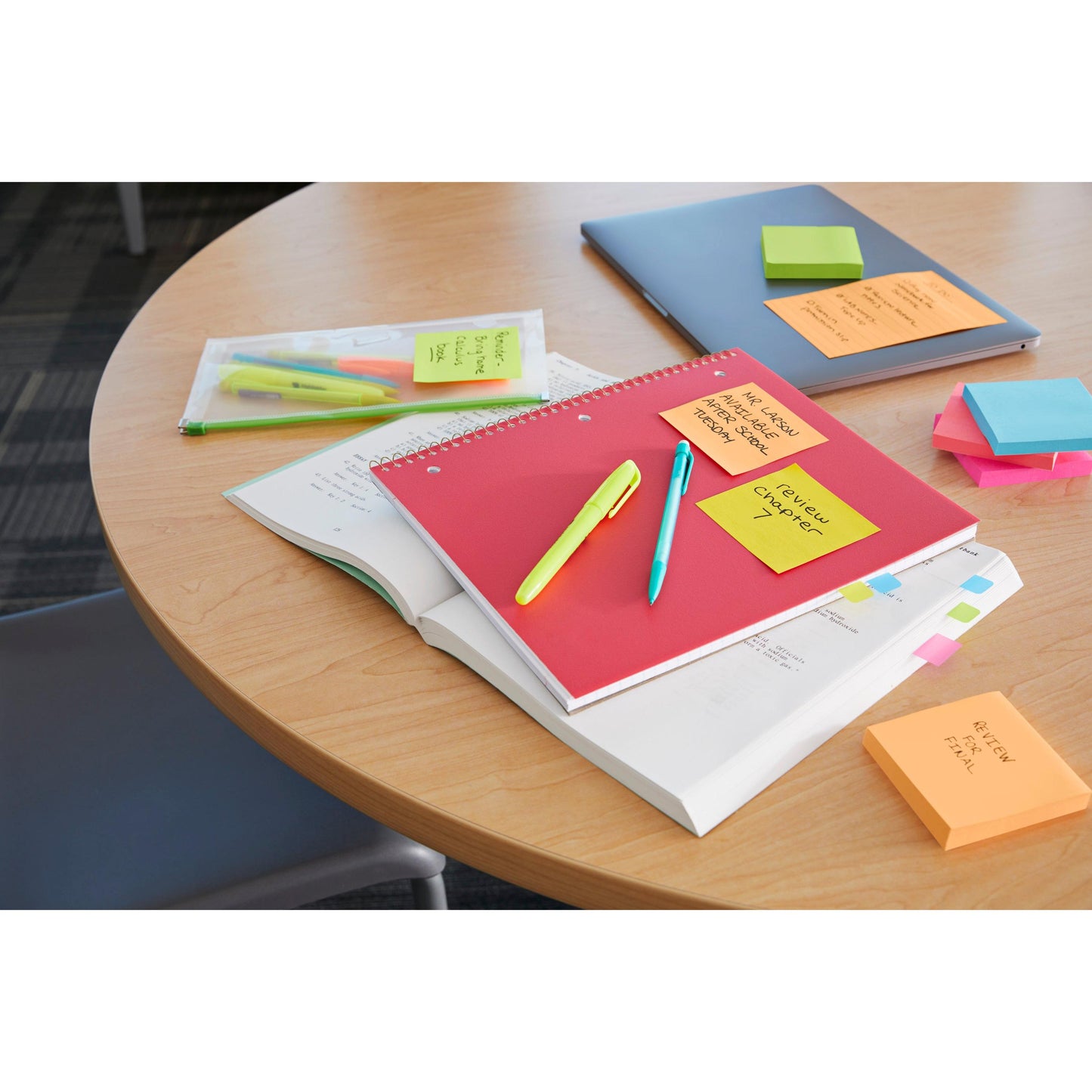 Ein runder Holztisch mit einem roten Notizbuch, einem aufgeschlagenen Lehrbuch, Stiften, Textmarkern, einem Laptop, einer Klarsichttasche und 3M Deutschland GmbH Post-it® Super Sticky Z-Notes (Boost Collection, 76x76mm) ist zu sehen; ein Stuhl ist teilweise abgebildet.