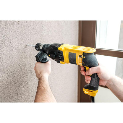 Henkilö poraa musta-keltaisella porakoneella beigeen seinään, kun lähellä näkyy 3M Deutschland GmbH:n Scotch® Extremium™ Ultra High Performance -teippi DT17 (10 m x 24 mm, 1 rulla); taustalla näkyy käsiä ja osa oven tai ikkunan karmista.