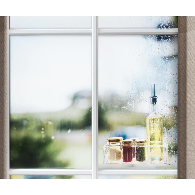 Ikkuna, jossa on sadepisaroita, näyttää ulkokohtauksen. Ikkunalaudalla on öljypullo, kolme pientä lasia kultaisilla kansilla ja rulla Scotch-FIX™ läpinäkyvää kaksipuolista kiinnitysteippiä 4910C 3M Deutschland GmbH:ltä.