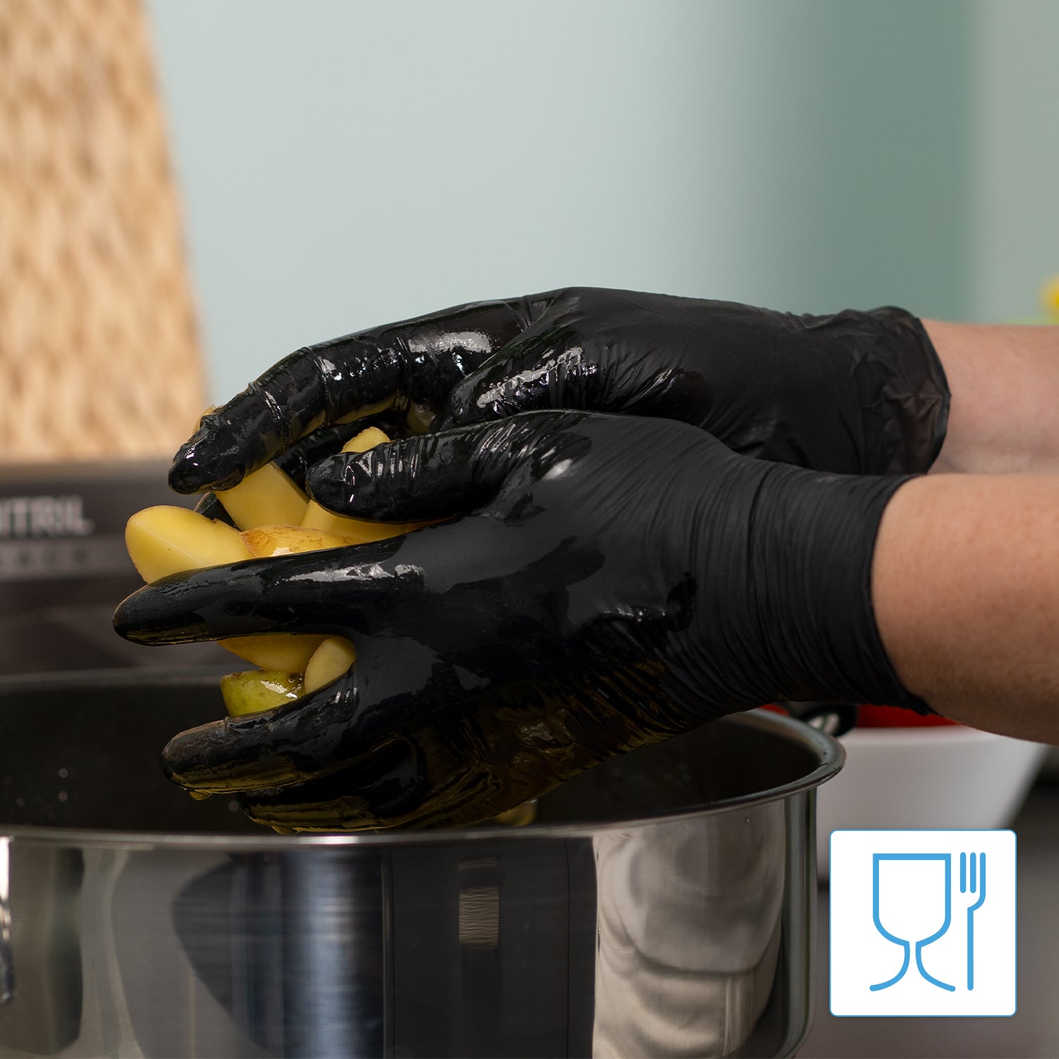 Eine Person mit ARNOMED NITRIL BLACK 200er Nitrilhandschuhe Schwarz der ARNOWA GmbH hält gelbe Paprika über einen Edelstahltopf. Die latex- und puderfreien Handschuhe sorgen für einen sicheren Umgang mit Lebensmitteln; Utensilien- und Glassymbole erscheinen in der Bildecke.