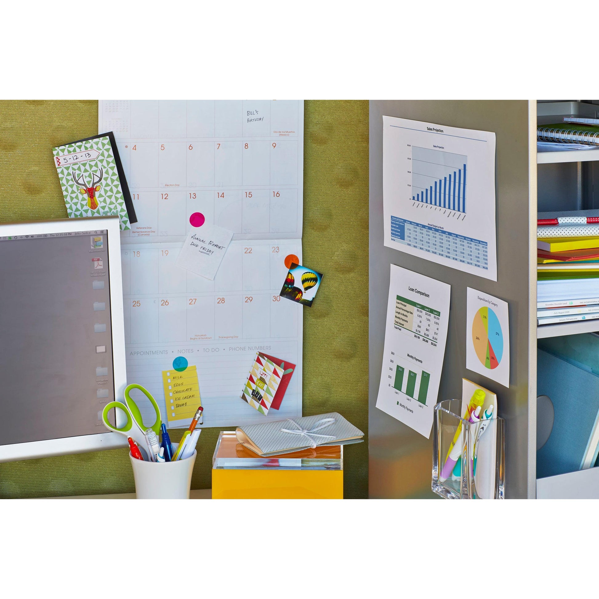 Ein Arbeitsplatz mit Tabellen, einem Computermonitor, bunten Schreibwaren, Büchern in Regalen und Haftnotizen, die mit Scotch-FIX™ Ablösbare Montagequadrate 108-ST64-P (12,7 mm x 12,7 mm, 64 Stück/Packung) von 3M Deutschland GmbH befestigt sind. Stifte und Notizkarten liegen auf dem Schreibtisch.