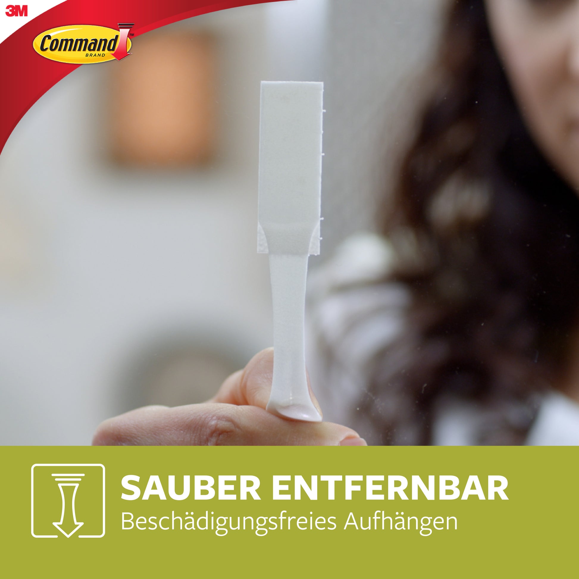 Eine Person hält einen weißen Klebestreifen mit Lasche. Das Command-Logo befindet sich oben links. Darunter steht der Text: "Sauber entfernbar. Beschädigungsfreies Aufhängen." Produkt: Große Command™ Bilder-Montage Strips L, 6 Sets, 3M Deutschland GmbH.