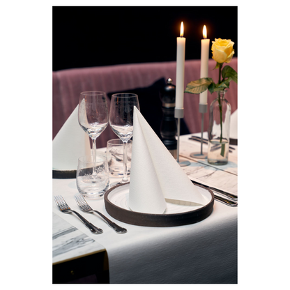 Ruokapöytä on elegantisti katettu kahdella Duni Dunilin®-lautasliinalla 48 x 48 cm Valkoinen, jotka on taiteltu kolmioksi lautasille. Kaksi suurta palavaa kynttilää ja keltainen ruusu lasimaljakossa koristavat taustaa. Viinilasit, vesilasi ja aterimet täydentävät tämän vaativan ilmapiirin kangasmaista viehätystä.
