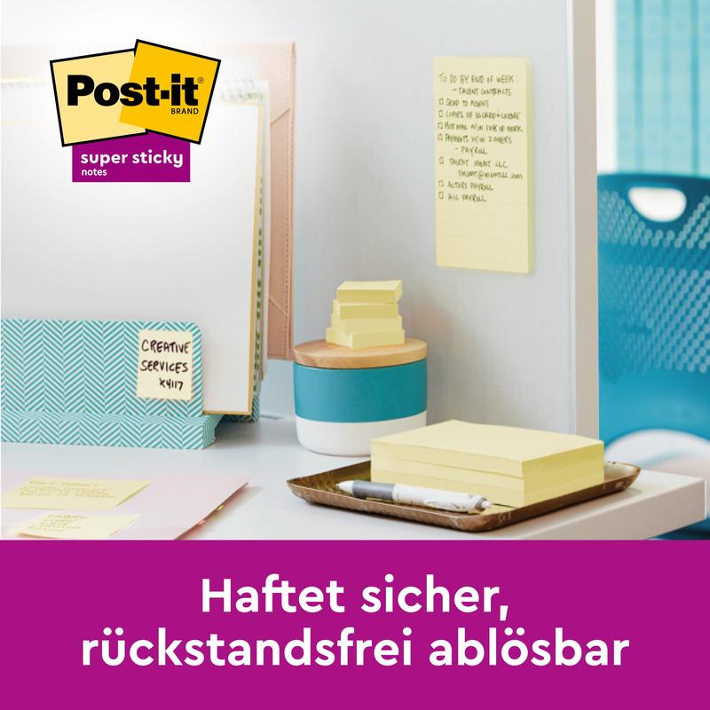 Kirjoituspöydällä on kansioita, kyniä ja pinoja 3M Post-it® Super Sticky 100% kierrätettyjä muistilappuja (76x76mm, 70 arkkia/lohko, PEFC). Keltainen lappu on kiinnitetty seinään. Saksankielinen teksti: "Kiinnittyy varmasti, irtoaa jäämättömästi."