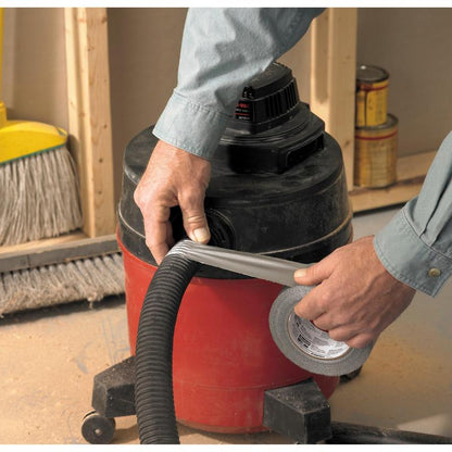 Henkilö käärii Scotch® Universal Teippiä 2904 (50 m x 48 mm) 3M Deutschland GmbH:lta pölynimurin letkun ympärille, joka on kiinnitetty punaiseen työpajaimuriin. Taustalla näkyy luuta ja maalipurkkeja.