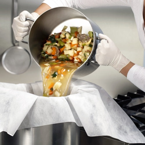 Valkoisilla hansikkailla varustettu henkilö kaataa vihanneksia ja lientä pergamentilla vuorattujen siivilä- ja suodatinkankaiden (100x100 cm, 10 kappaletta) kautta Starpakilta suureen metallisäiliöön ja esittelee näin käytännön sovellusta keittiössä.