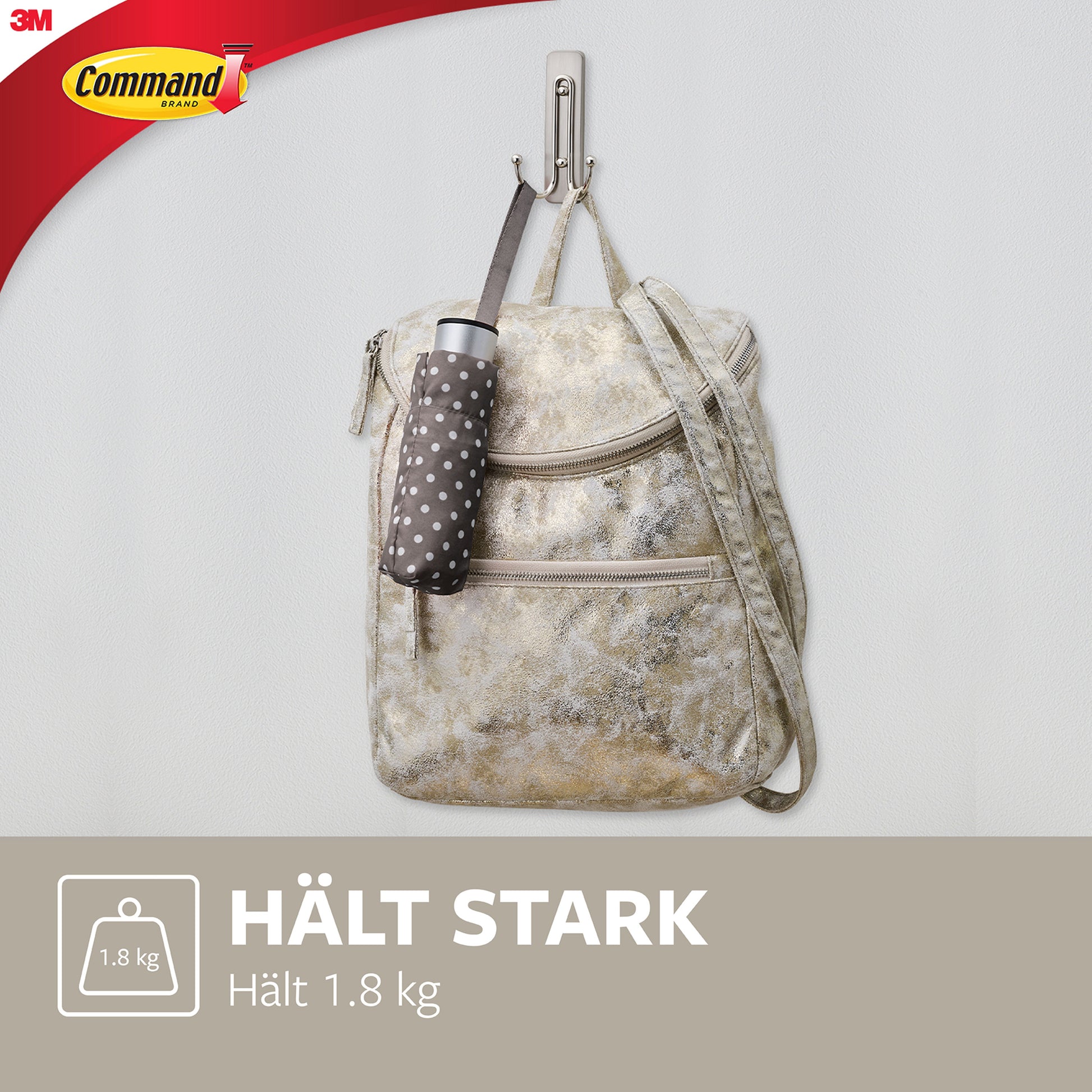 Ein großer Command™ Doppelhaken in gebürstetem Nickel von 3M Deutschland GmbH hält einen beigen Rucksack und einen gepunkteten Regenschirm an einer weißen Wand. Das Bild zeigt das 3M-Logo und den Hinweis: Tragkraft bis zu 1,8 kg.