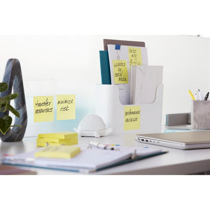 Siisti toimistopöytä, jossa on 3M Deutschland GmbH:n Post-it® Super Sticky Notes (76x127 mm, 90 arkkia, 100 % PEFC) lasierottimen päällä, sekä kansiot pidikkeessä, kilpikonnafiguuri, toimistotarvikkeita, suljettu kannettava tietokone ja avoin muistikirja kynän kanssa.