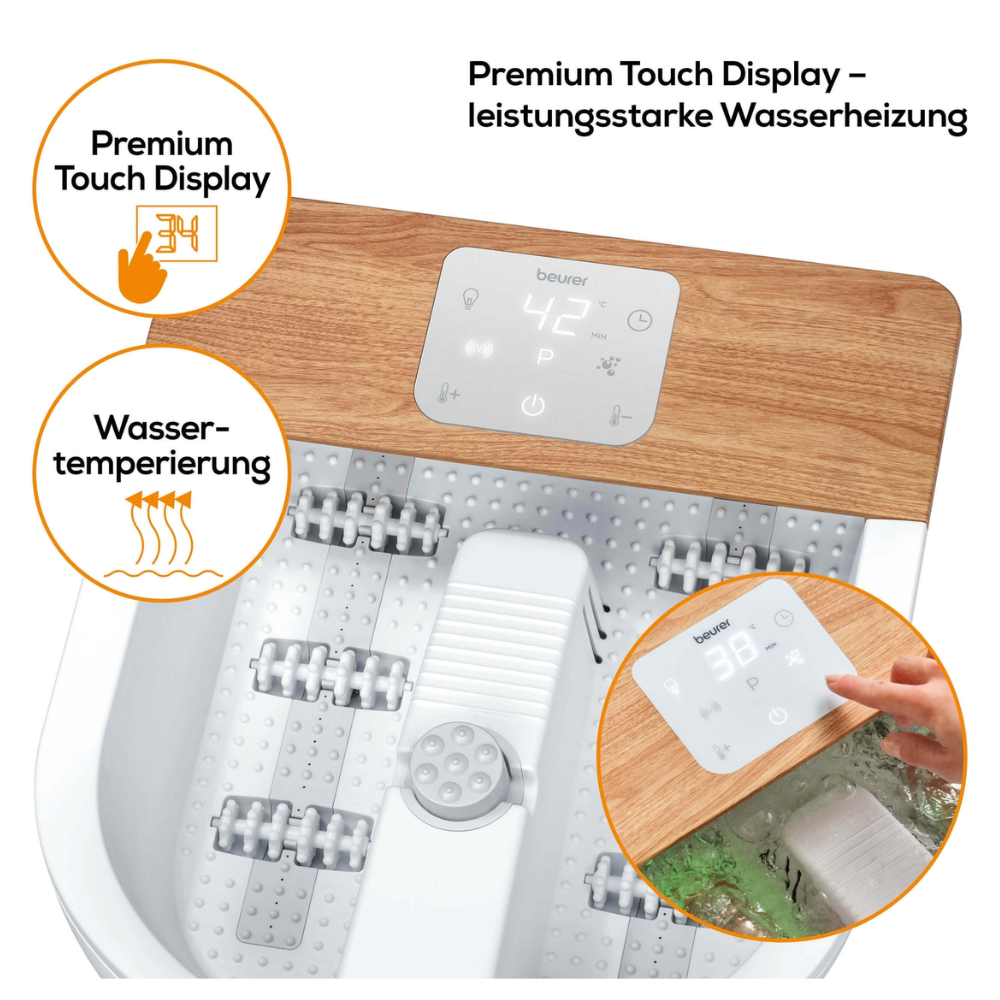 Jalkakylpy merkiltä Beurer FB 65 Wellness -jalkakylpylä Beurer GmbH:ltä, jossa on valkoinen pohja ja puulevy, sekä digitaalinen kosketusnäyttö, joka näyttää lämpötilaksi 42 °C. Etiketeissä lukee 'Veden lämpötilansäätö' ja 'Premium kosketusnäyttö'. Käsi säätää näyttöä ja hierontarullat värähtely- ja porehierontaan ovat näkyvissä.