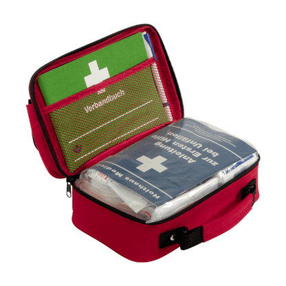 Kompakti punainen Holthaus Verbandtasche Office plus, DIN 13 157 Holthaus Medical GmbH & Co. KG:ltä, mustalla kahvalla, joka voidaan avata paljastamaan sisältö. Sisällä on vihreä käyttöohje ja sininen Holthaus Verbandtasche, joka on koristeltu valkoisella ristillä ja saksankielisellä tekstillä. Ensiapuvälineet on selkeästi järjestetty verkkotaskuihin ja lokeroihin, mikä tekee siitä ihanteellisen toimistoympäristöihin.