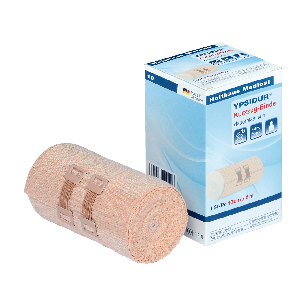 Ypsidur® lyhytvetoside kiinnitysklipsillä Holthaus Medical GmbH & Co. KG:ltä. Kuvassa näkyy rullattu pysyvästi elastinen lyhytvetoside laatikkonsa vieressä. Beige side on kiinnitetty kahdella beigellä kiinnitysklipsillä, ja laatikon teksti on pääosin saksaksi ja sisältää tuotetietoja.
