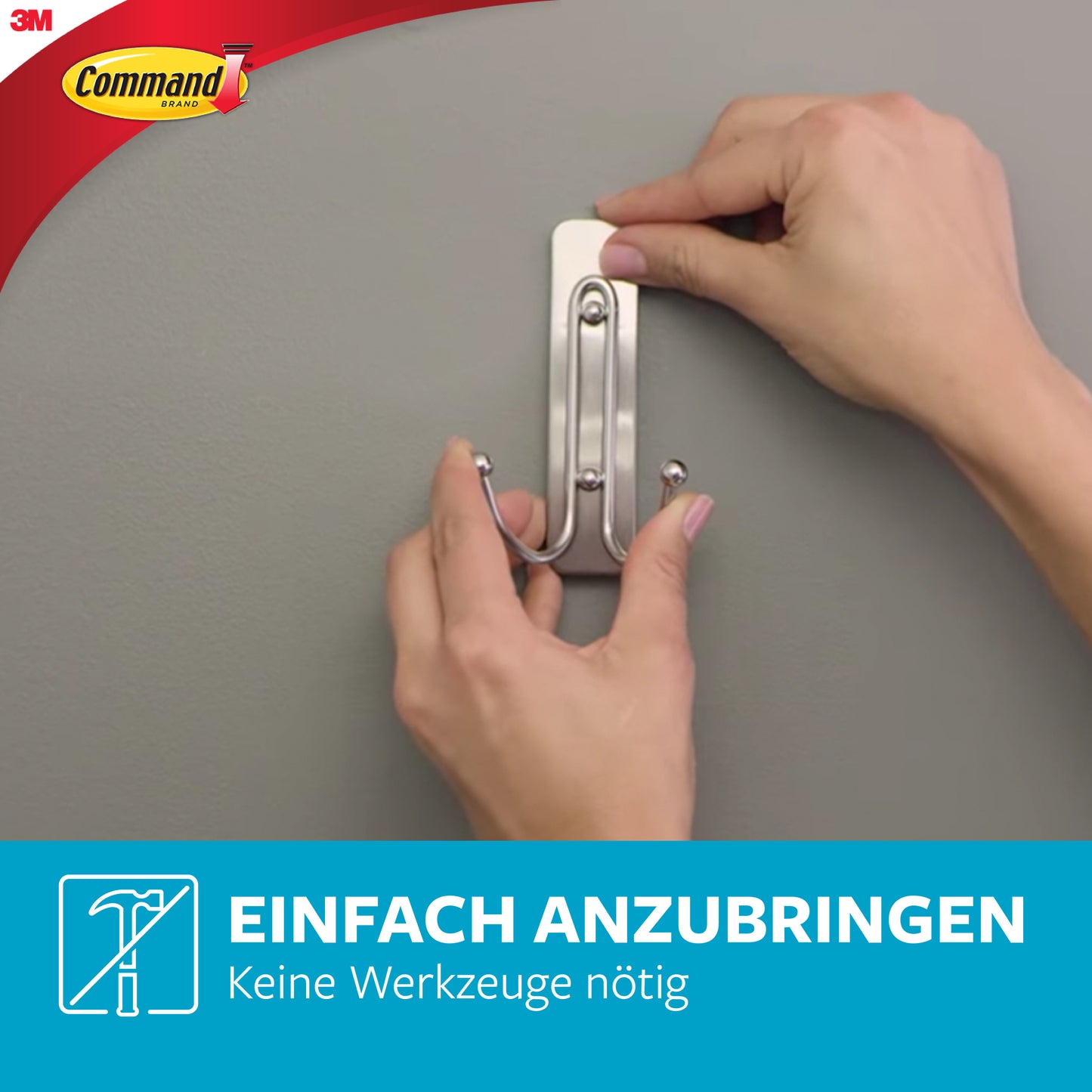 Eine Person bringt einen 3M Command™ Großer Badezimmer-Doppelhaken Nickel satiniert an einer grauen Wand an - ganz ohne Bohren. Im Bild sind das Command-Logo und der Text "Einfach anbringen, keine Werkzeuge nötig - ideal als Handtuchhaken" zu sehen.