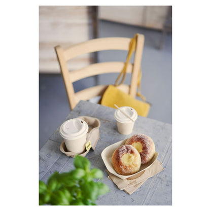 Pöydällä on tarjottimella kaksi sokerilla päällystettyä leivonnaista ja kaksi kannella varustettua Duni Kaffeebecher 'Sweet Painettu Bagasse' -mukia Duni GmbH:lta. Keltainen käsilaukku roikkuu puutuolilla, kun taas osittain näkyvä vihreä kasvi etualalla korostaa hienovaraisesti kestävyyden teemaa.